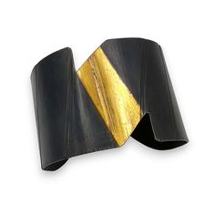 Gold & Steel Bracelet - This sculptural steel cuff boasts a striking contrast in both color and texture that creates a play of light, enhancing its curved, ribbon-like form with a smooth, gently flowing black surface. The top of the cuff features lustrous 24k gold foil applied using a variation of the ancient Korean technique of Keum-Boo. Modern Twist Cuff Bracelet For Formal Occasions, Modern Evening Cuff Bracelet, Contemporary Cuff Bangle For Formal Occasions, Modern Black Cuff Bracelet For Parties, Keum Boo, Artful Home, Steel Bracelet, Gold Foil, Precious Metals