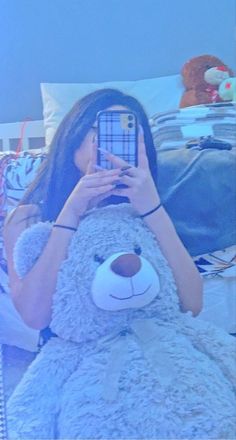 a woman taking a selfie with her phone next to a large teddy bear on a bed