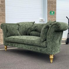 a green couch sitting on top of a parking lot next to a garage door with roller doors in the background