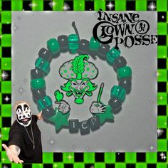 a person wearing a mask and holding onto a green beaded bracelet with an image of a skull on it