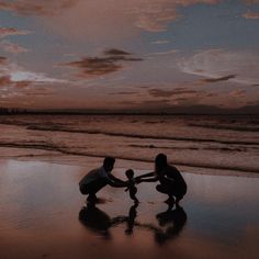 two people on the beach playing with a baby in front of an ocean at sunset