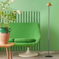 a green couch and table with a potted plant on it in front of a green wall