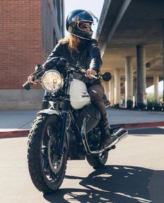 a man riding on the back of a motorcycle down a street next to a tall building