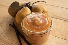 two apples sit next to a jar of cinnamon butter on a wooden table with sticks