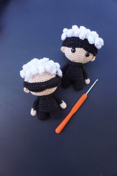 two crocheted dolls sitting on top of a table next to a knitting needle