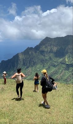 four people standing on top of a grass covered hill with mountains in the background and clouds in the sky