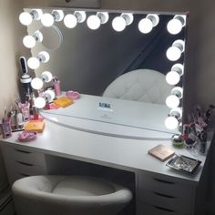 a white vanity with lights on it and a stool in front of the mirror,