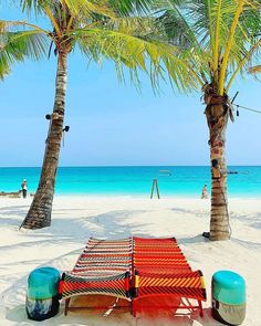 a hammock and two stools are on the beach near some palm trees