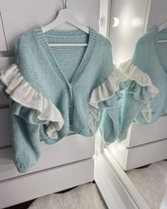 a blue sweater with ruffles is hanging on a white hanger in front of a mirror