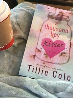 a cup of coffee next to a book titled a thousand boy kisses by tillie cole