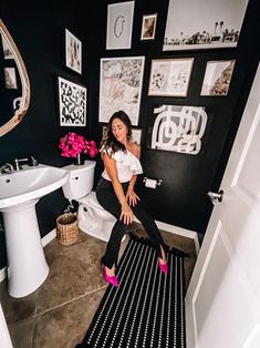 a woman sitting on top of a toilet in a bathroom next to a white sink