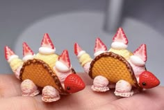 three tiny toy food items are placed on someone's hand, one has strawberrys and the other has strawberries