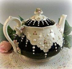 a black and white tea pot with pearls on the top sits on a lace doily