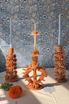 three candles sitting on top of a table next to orange flowers and blue wallpaper