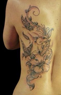 a woman's back tattoo with flowers and butterflies on her left side ribcage