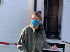 a woman wearing a face mask standing in front of a trailer