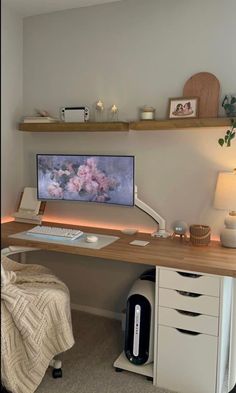 a desk with a computer on top of it and shelves above the desk, along with other items