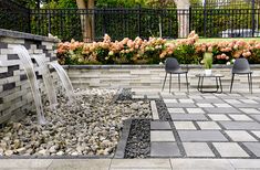 an outdoor patio with a fountain and seating area next to flowers on the side walk