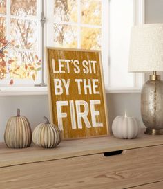 a wooden sign that says let's sit by the fire next to some pumpkins