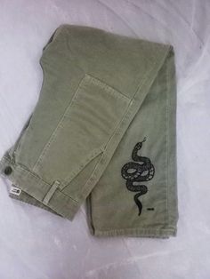 a pair of green shorts with a snake embroidered on the front and side, sitting on a white sheet