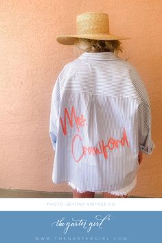 the back of a woman's shirt with writing on it and a straw hat