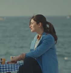 a woman sitting at a table on the beach with a cup of coffee in her hand