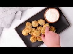 a black plate topped with tater tots next to a bowl of ranch dressing