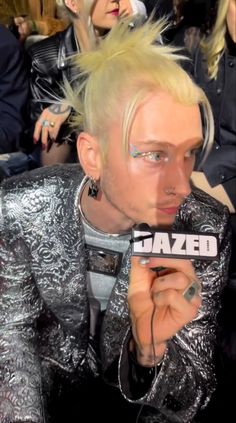 a man with blonde hair and piercings holding a microphone in front of his face