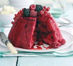 a red velvet cake with berries on top is sitting on a plate next to a knife and fork