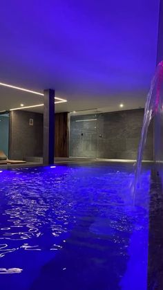 an indoor swimming pool with blue lighting and water feature in the center, surrounded by stone walls