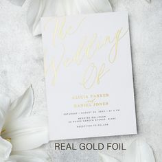 a white and gold wedding card on top of flowers with the words, the wedding off