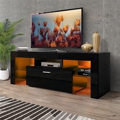 a flat screen tv sitting on top of a black entertainment center next to a potted plant