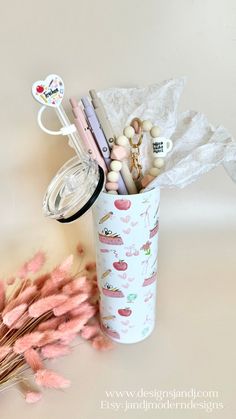 a cup filled with lots of different items next to pink flowers