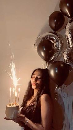 a woman holding a cake with sparklers on it in front of balloons and streamers