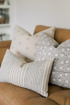 three pillows sitting on top of a brown couch