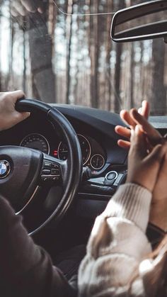 a person driving a car in the woods with their hands on the steering wheel and one hand on the dashboard