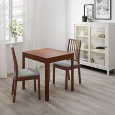 a table and two chairs in a room with white walls, hardwood floors and windows