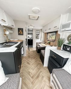 the interior of an rv with wood flooring and white cabinets, black appliances and counter tops