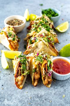 some tacos are sitting on a table with dipping sauces and lime wedges