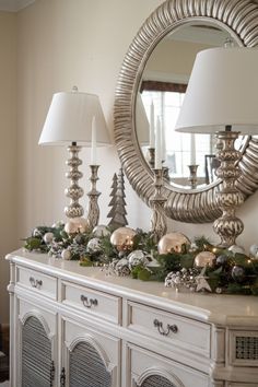 a white dresser with christmas decorations on top and a large mirror above it, along with two lamps