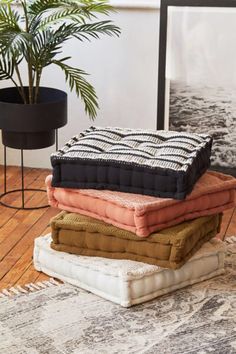 a pile of blankets sitting on top of a wooden floor next to a potted plant