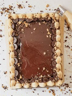 a square cake with chocolate frosting surrounded by crumbs