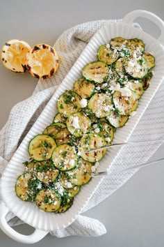 zucchini with cheese and herbs on a white platter next to an orange