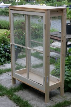 a wooden box with glass inside sitting on the ground in front of some plants and flowers