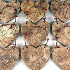 several wooden hearts with red berries hanging from strings on a white background, each heart shaped like a leaf