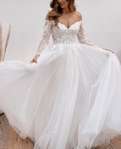 a woman in a white wedding dress with long sleeves and sheer tulle skirt is posing for the camera