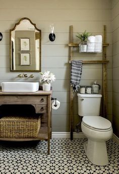 a white toilet sitting next to a sink in a bathroom under a mirror and wooden shelf