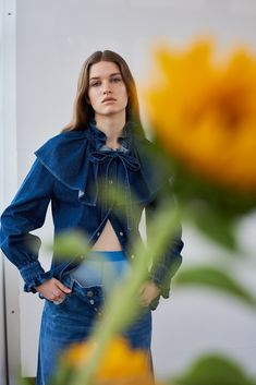 a woman standing in front of a sunflower with her hands on her hips and looking at the camera