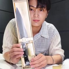 a young man holding a knife in front of his face while sitting at a table