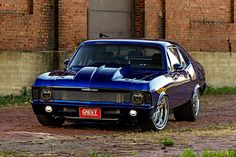 a blue muscle car parked in front of a brick building